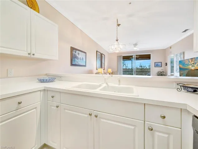 Kitchen featuring light countertops, ornamental molding, a sink, and white cabinets