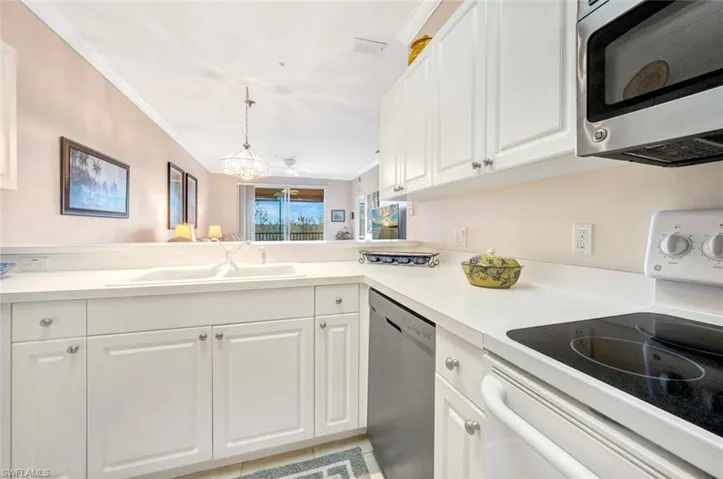 Kitchen featuring light countertops, appliances with stainless steel finishes, ornamental molding, white cabinetry, and a sink
