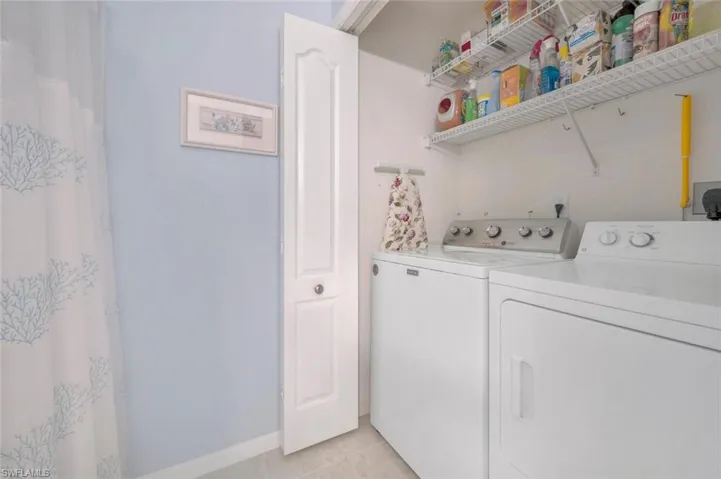 Clothes washing area featuring light tile patterned floors, laundry area, independent washer and dryer, and baseboards
