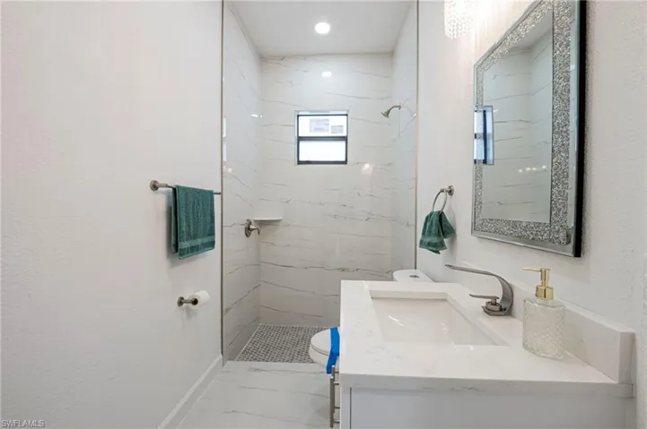 Full bath featuring vanity, a marble finish shower, and a textured wall