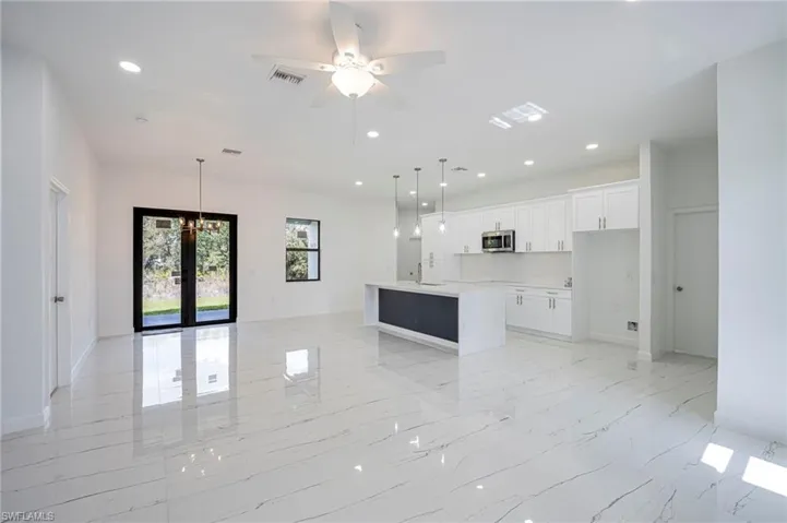Kitchen with open floor plan, a ceiling fan, white cabinets, a kitchen island with sink, and a chandelier