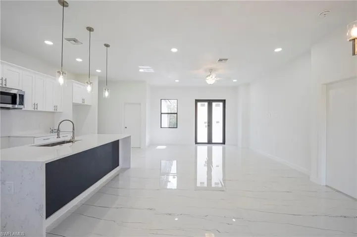 Kitchen featuring decorative light fixtures, light stone counters, stainless steel microwave, white cabinets, and open floor plan