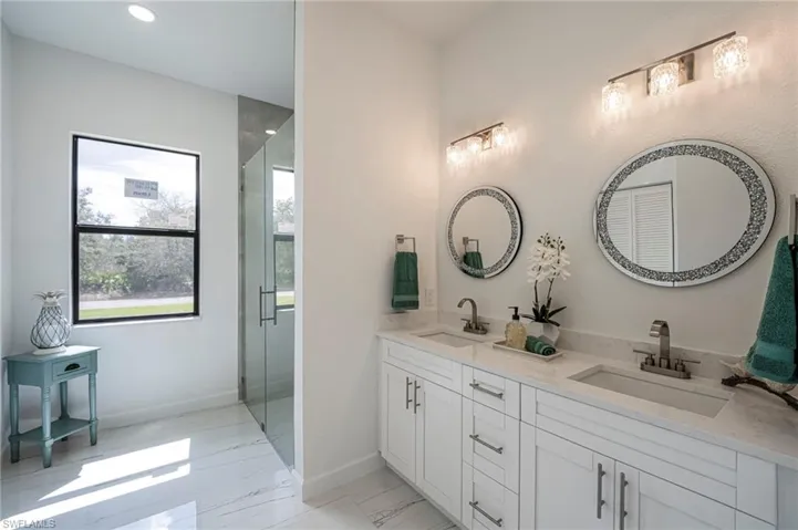 Bathroom featuring double vanity, a stall shower, and light marble finish flooring