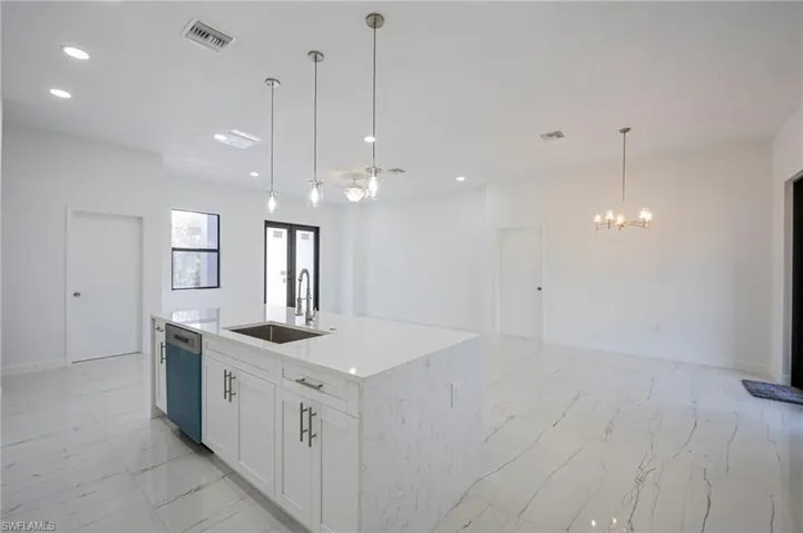 Kitchen with light stone countertops, white cabinets, an island with sink, open floor plan, and dishwasher