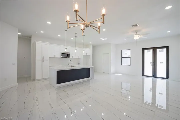 Kitchen featuring open floor plan, a chandelier, white cabinets, a kitchen island with sink, and light stone counters