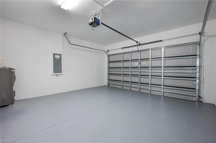 Garage featuring electric water heater, electric panel, and a garage door opener