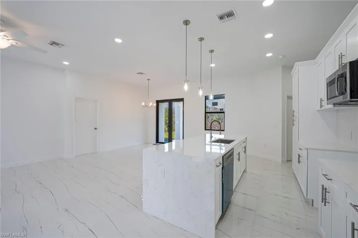 Kitchen with light stone countertops, white cabinets, ceiling fan, a kitchen island with sink, and stainless steel appliances