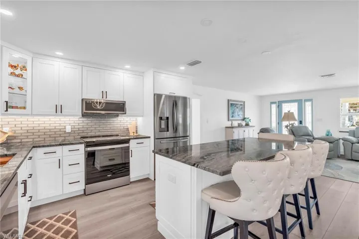 Kitchen featuring white cabinetry, glass tile backsplash, stainless steel appliances, and a breakfast bar - VIRTUALLY ENHANCED