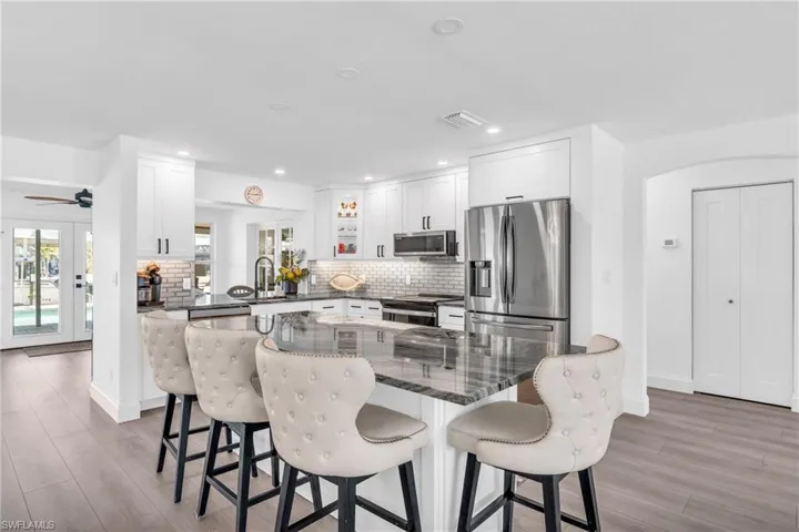 Kitchen featuring white cabinetry, glass tile backsplash, stainless steel appliances, and a breakfast bar - VIRTUALLY ENHANCED