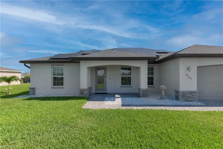 Rear view of property featuring a garage, a lawn, and solar panels