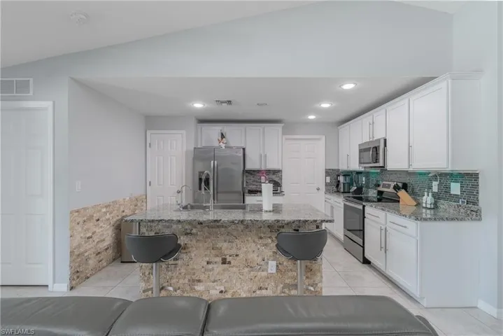 Kitchen with a kitchen breakfast bar, light tile floors, tasteful backsplash, and appliances with stainless steel finishes