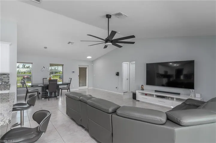 Living room with lofted ceiling, ceiling fan, and light tile floors