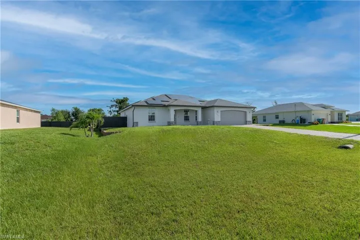 Ranch-style home with a garage, solar panels, and a front lawn