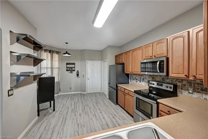 Kitchen featuring decorative backsplash, light wood-type flooring, decorative light fixtures, and appliances with stainless steel finishes