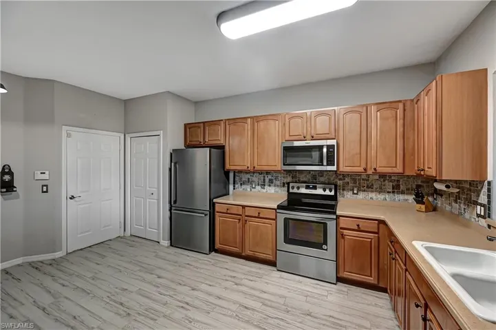 Kitchen featuring backsplash, light wood-type flooring, sink, and appliances with stainless steel finishes
