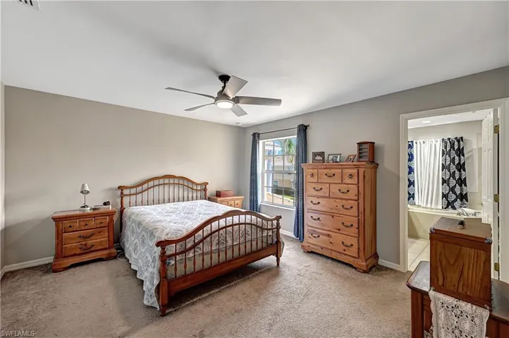Carpeted bedroom with connected bathroom and ceiling fan