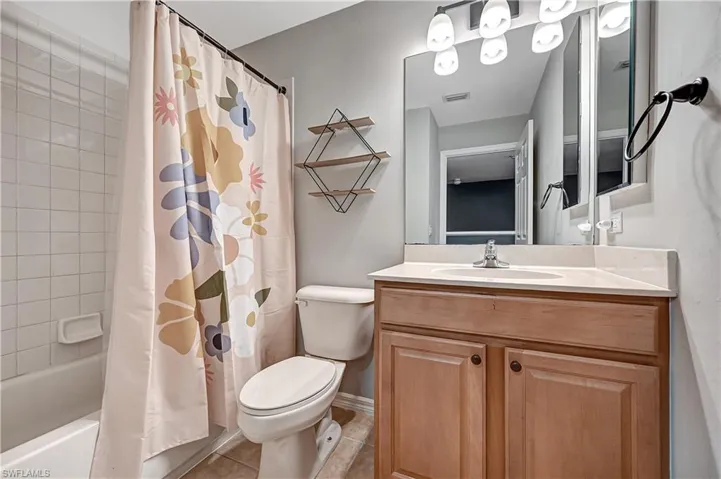Full bathroom with tile patterned floors, shower / bath combination with curtain, toilet, and vanity