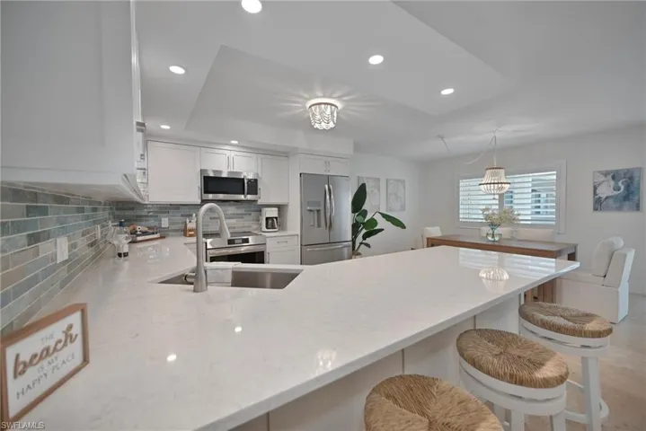 Kitchen with a peninsula, backsplash, white cabinetry, light stone counters, and stainless steel appliances