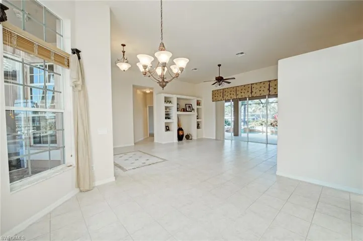 Tiled empty room featuring ceiling fan with notable chandelier and built in shelves