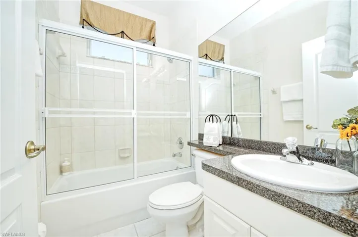 Full bathroom with tile patterned floors, vanity, enclosed tub / shower combo, and toilet
