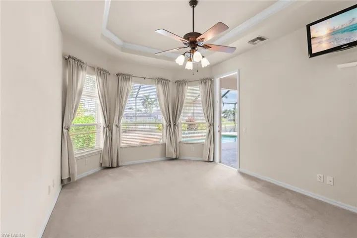 master bedroom with light carpet, a tray ceiling, and ceiling fan