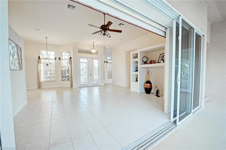 Unfurnished living room featuring ceiling fan with notable chandelier, light tile patterned flooring, built in shelves, and french doors