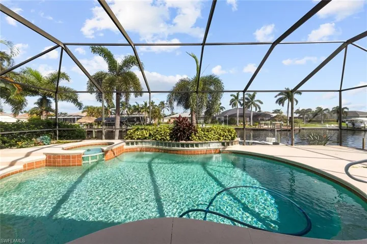 View of swimming pool featuring glass enclosure, a water view, a patio, and an in ground hot tub