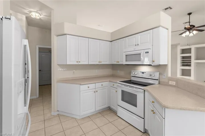 Kitchen with ceiling fan, white cabinets, light tile patterned floors, and white appliances
