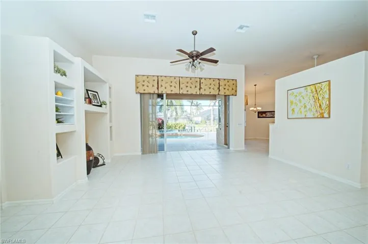 Spare room featuring ceiling fan with notable chandelier, built in features, and light tile patterned floors