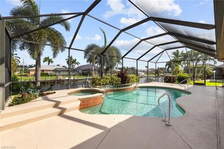 View of pool with a water view, an in ground hot tub, a patio area, and glass enclosure