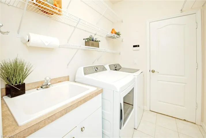 Laundry area featuring washer and clothes dryer, light tile patterned floors, cabinets, and sink