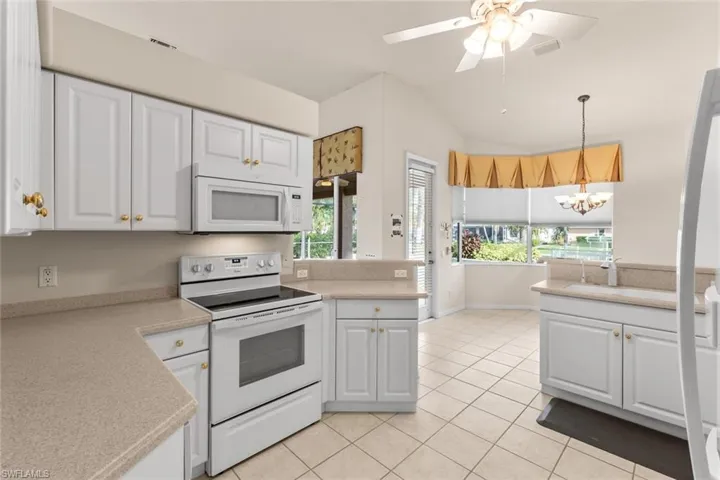 Kitchen featuring white appliances, white cabinetry, and a healthy amount of sunlight