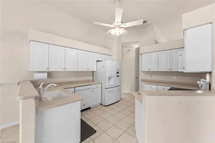 Kitchen with ceiling fan, white cabinets, sink, kitchen peninsula, and white appliances