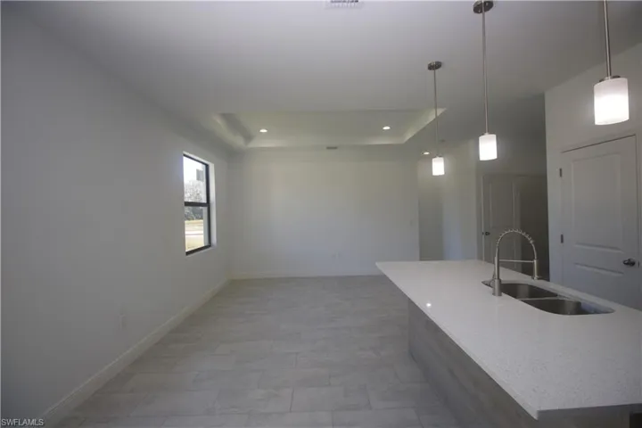 Kitchen featuring light stone countertops, sink, pendant lighting, a tray ceiling, and light tile patterned floors
