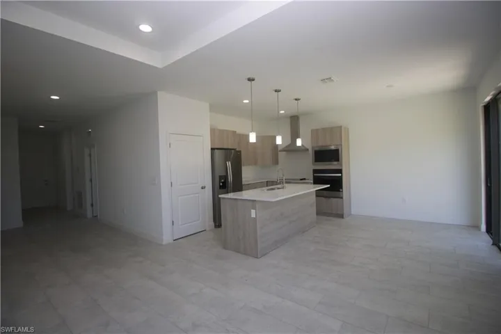 Kitchen with sink, wall chimney exhaust hood, hanging light fixtures, a kitchen island with sink, and appliances with stainless steel finishes