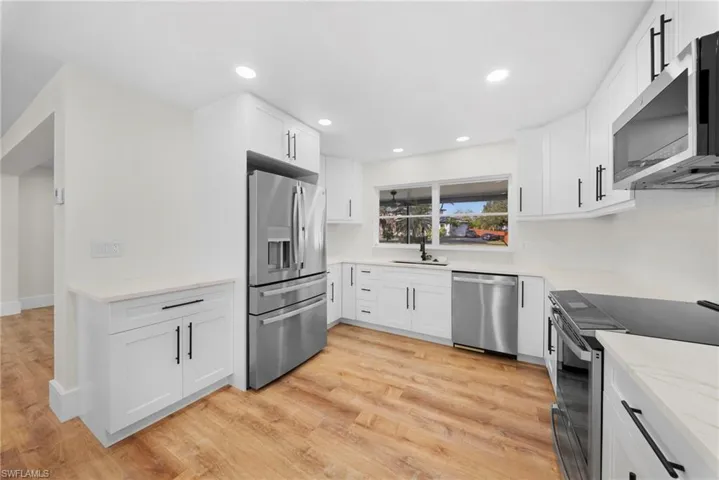 Kitchen featuring stainless steel appliances, light wood-style flooring, white cabinets, light stone counters, and recessed lighting