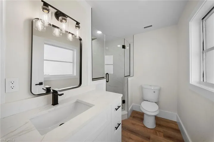 Full bath featuring a marble finish shower, vanity, and dark wood-style floors