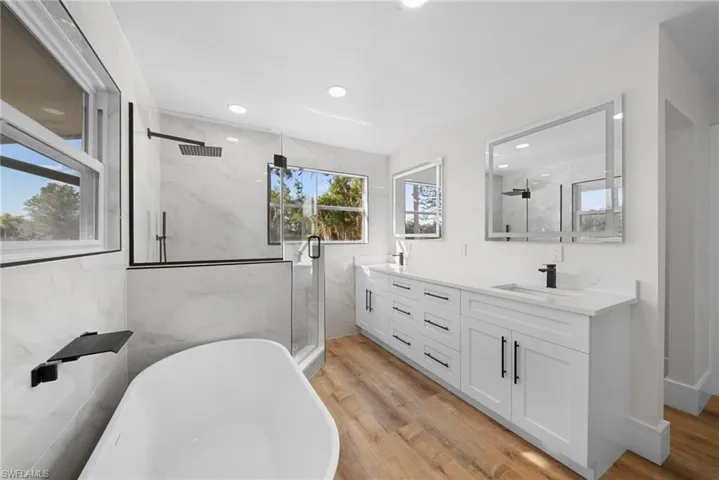 Full bathroom with plenty of natural light, double vanity, light wood-type flooring, a marble finish shower, and recessed lighting