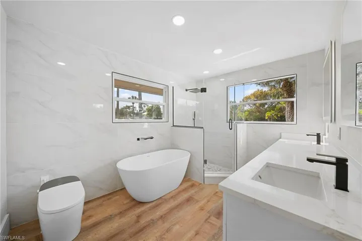 Bathroom with tile walls, a marble finish shower, double vanity, light wood finished floors, and a freestanding bath