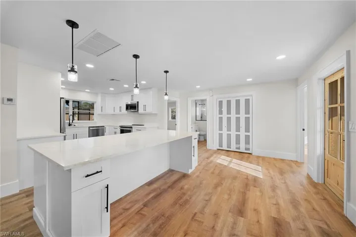 Kitchen featuring white cabinetry, light wood finished floors, light stone countertops, decorative light fixtures, and stainless steel appliances