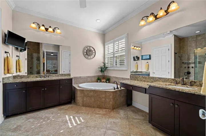 Bathroom featuring two vanities, a shower stall, a bath, ornamental molding, and a ceiling fan