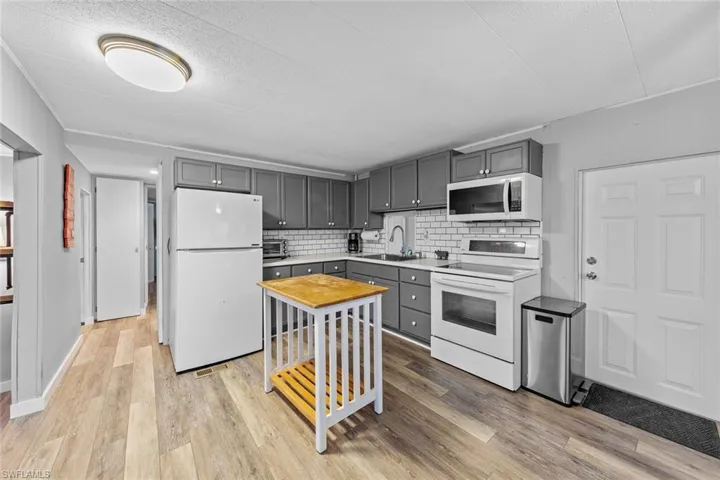 Kitchen featuring light wood-type flooring, backsplash, white appliances, sink, and gray cabinets