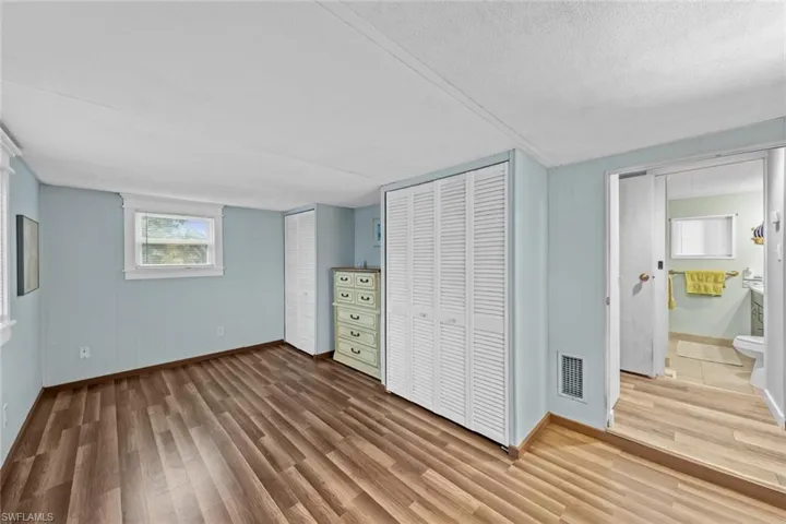 Unfurnished bedroom with a textured ceiling, hardwood / wood-style flooring, ensuite bath, and multiple closets
