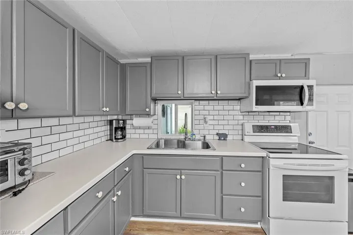 Kitchen with sink, electric range oven, backsplash, light hardwood / wood-style floors, and gray cabinets
