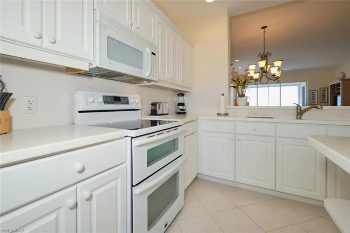 Kitchen featuring an inviting chandelier, white cabinets, light tile patterned floors, backsplash, and white appliances
