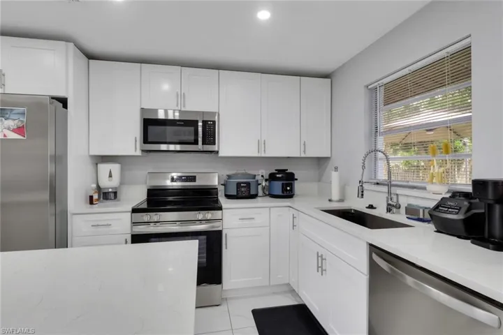 Modern kitchen featuring white cabinetry, stainless steel appliances, light-toned countertops, and a window with horizontal blinds