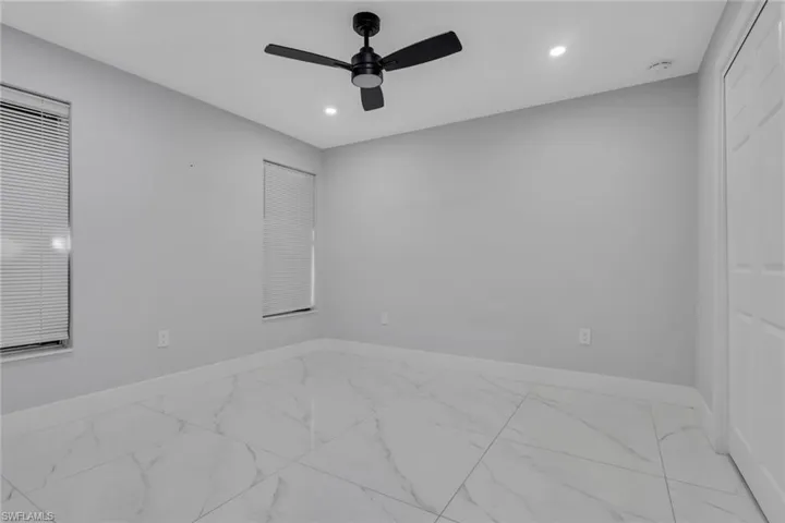 Spacious room featuring large format tile flooring, light gray walls, two windows with blinds, a ceiling fan, and recessed lighting