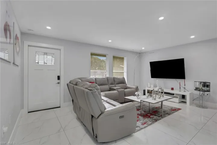 Bright living area featuring white tile flooring, recessed lighting, white walls, a white entry door with decorative glass inserts, and two windows providing natural illumination