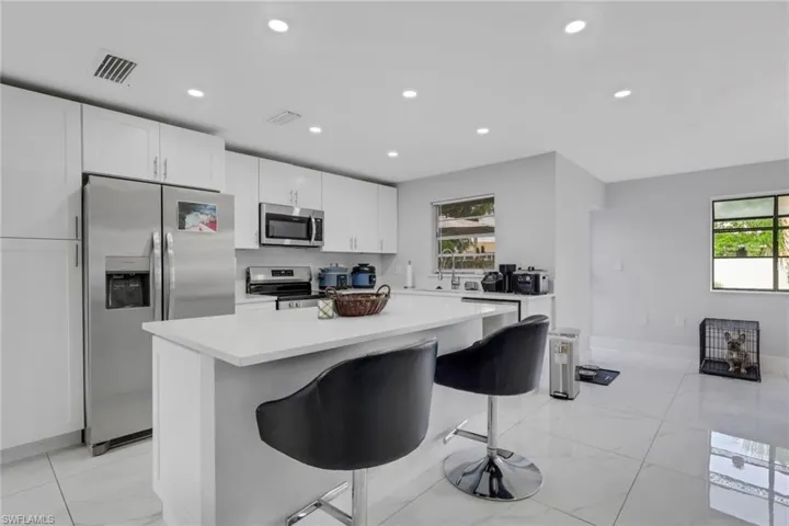 Contemporary kitchen featuring an island with seating, white shaker cabinetry, stainless steel appliances, and large format tile flooring
