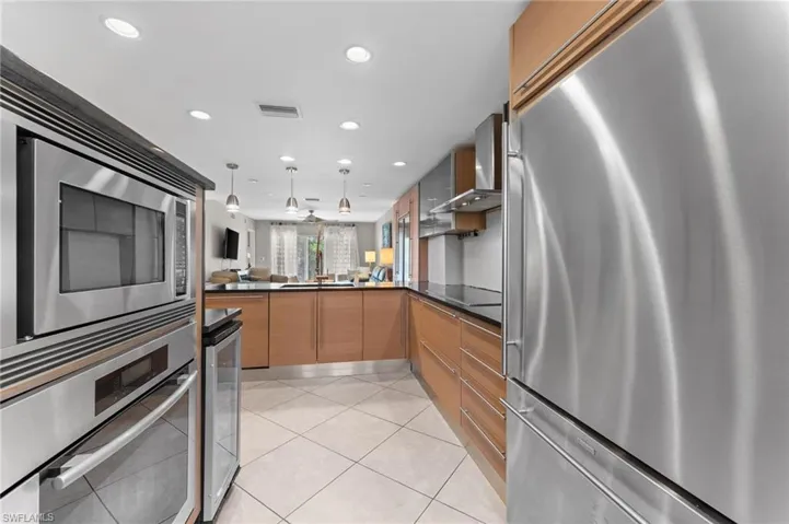 Kitchen featuring wall chimney exhaust hood, beverage cooler, stainless steel appliances, light tile patterned floors, and dark countertops